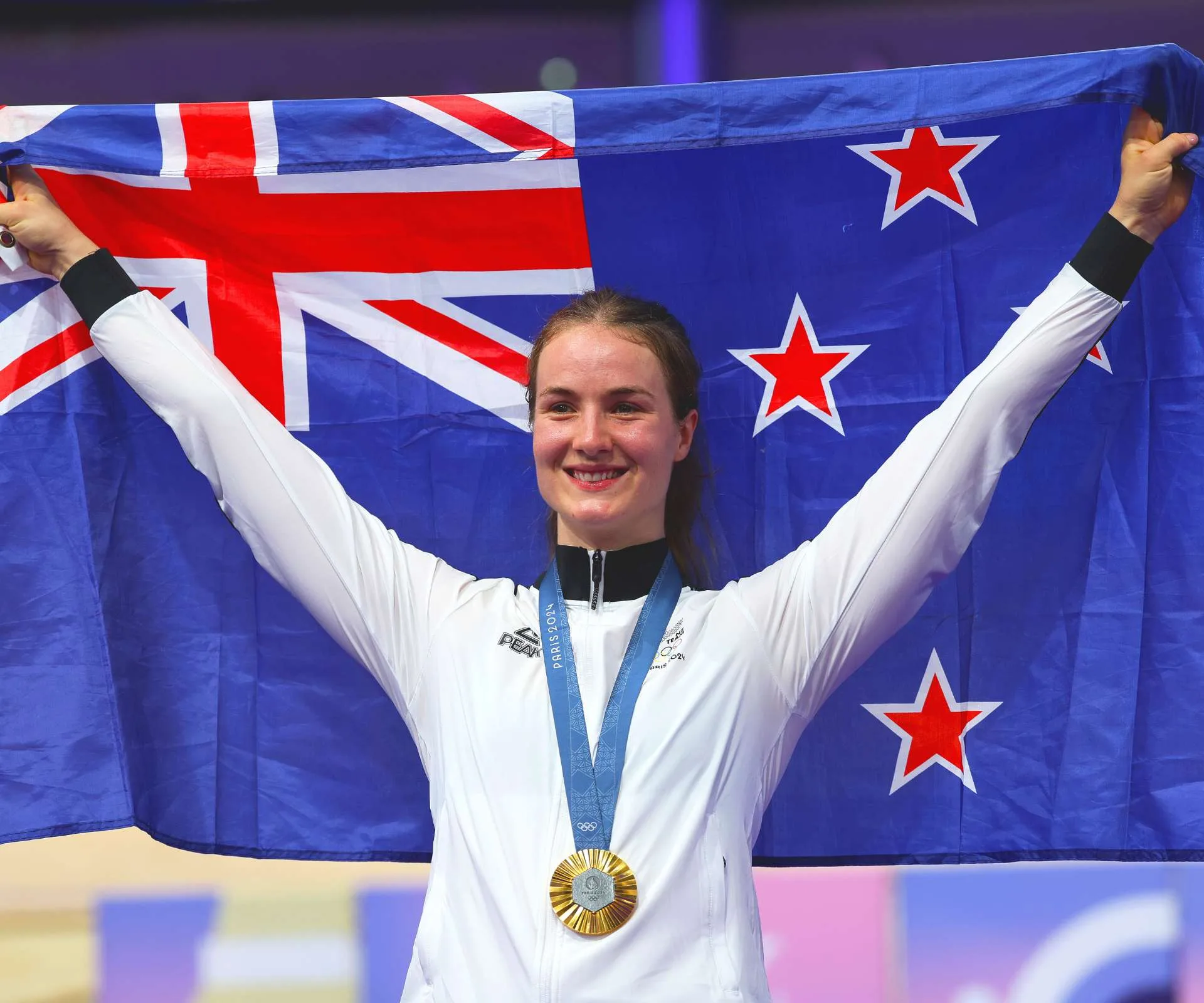 Ellesse Andrews holding an NZ flag up overhead after her 2024 Olympic win