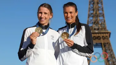 Brooke and Lucy holding up their 2024 Olympic medals in front of the Eiffel Tower