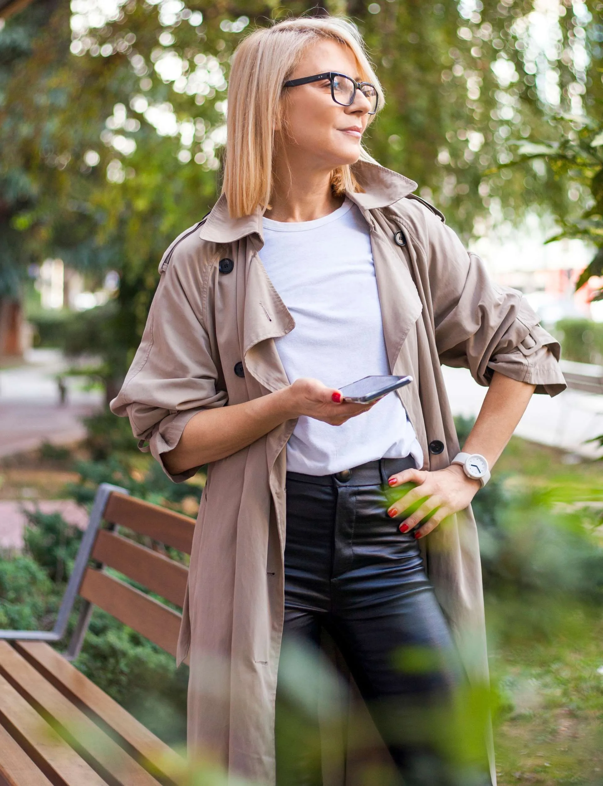 A woman looking to the side with one hand on her hip and the other holding a phone