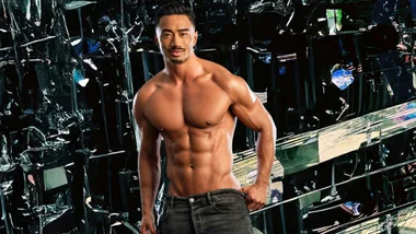 Michael shirtless in front of a black, reflective geometric wall