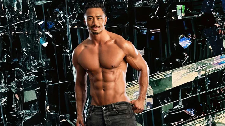 Michael shirtless in front of a black, reflective geometric wall