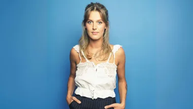Moana McArtney with her hands in her pockets in front of a blue backdrop