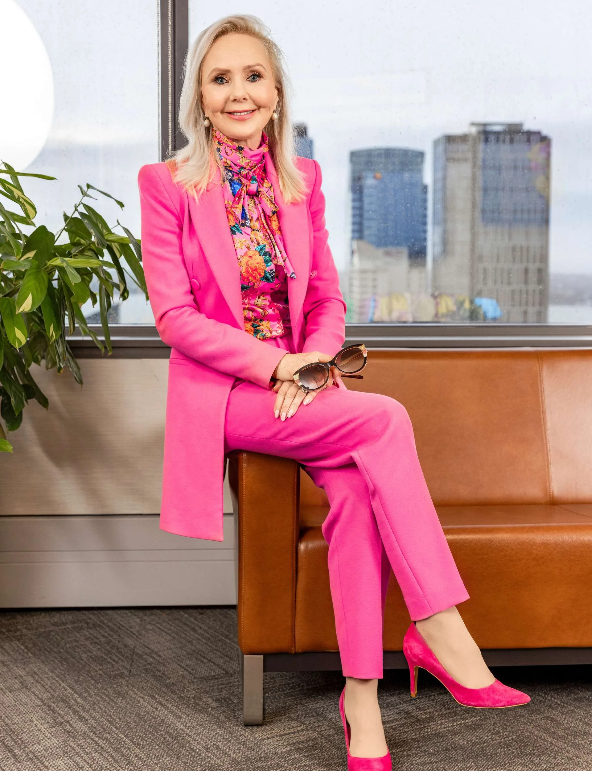 Sitting on the arm of a brown leather chair in a candy pink suit