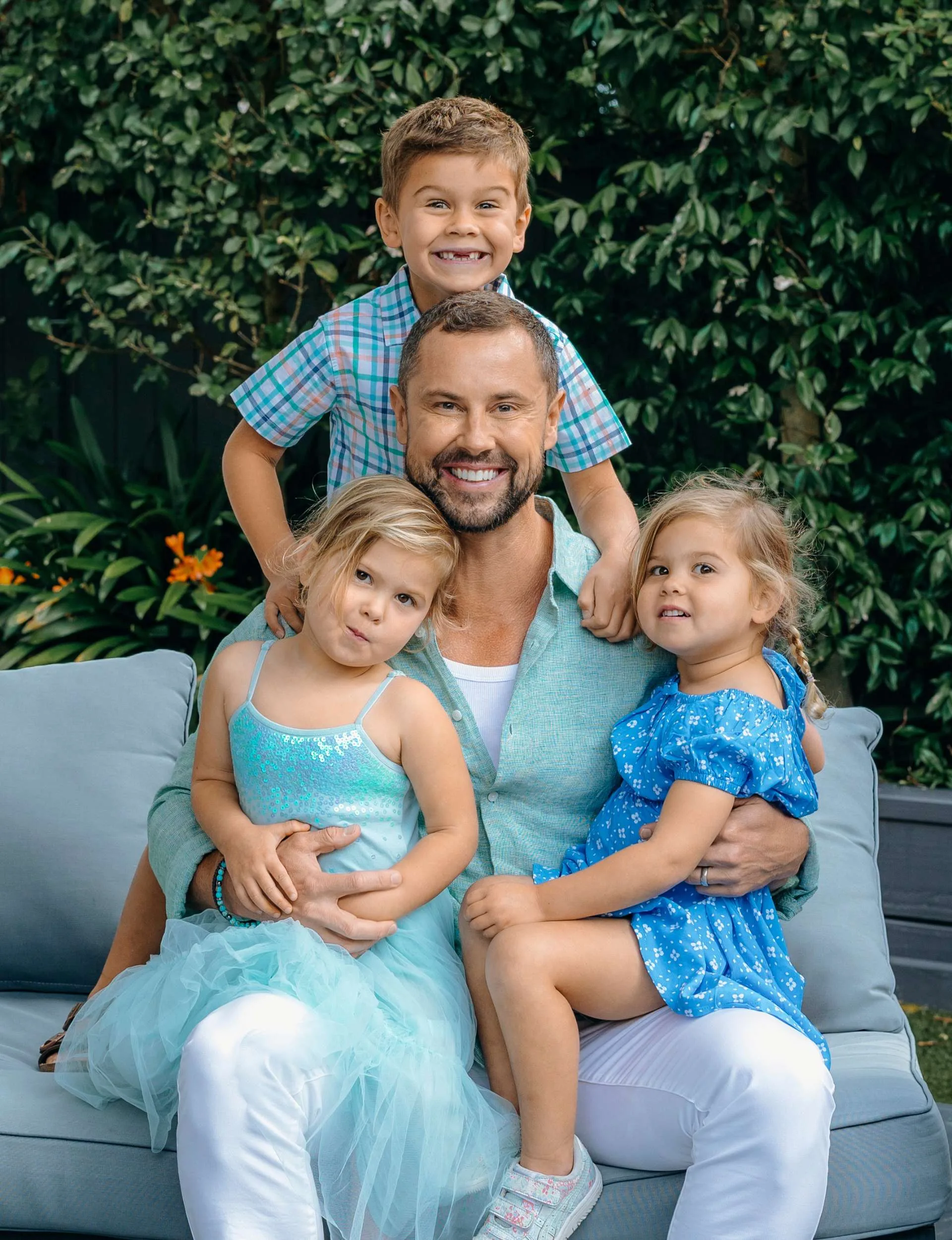 Sam sitting on an outdoor couch with his three kids climbing over him