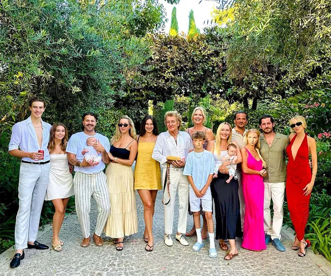 A large family gathered outdoors, smiling in a garden setting with lush greenery around them.