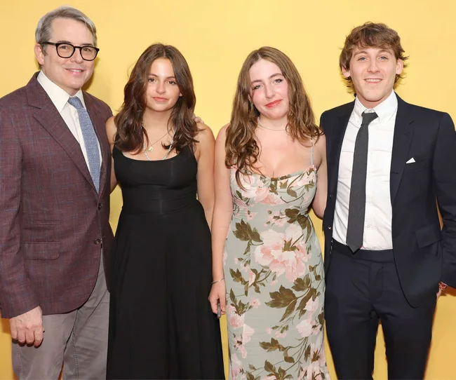 Four people posing together against a yellow background, dressed in formal and semi-formal attire.
