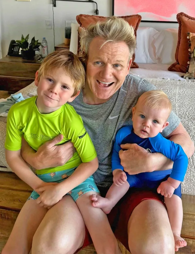 Gordon Ramsay sitting on the end of a bed with each of his sons on each of his knees