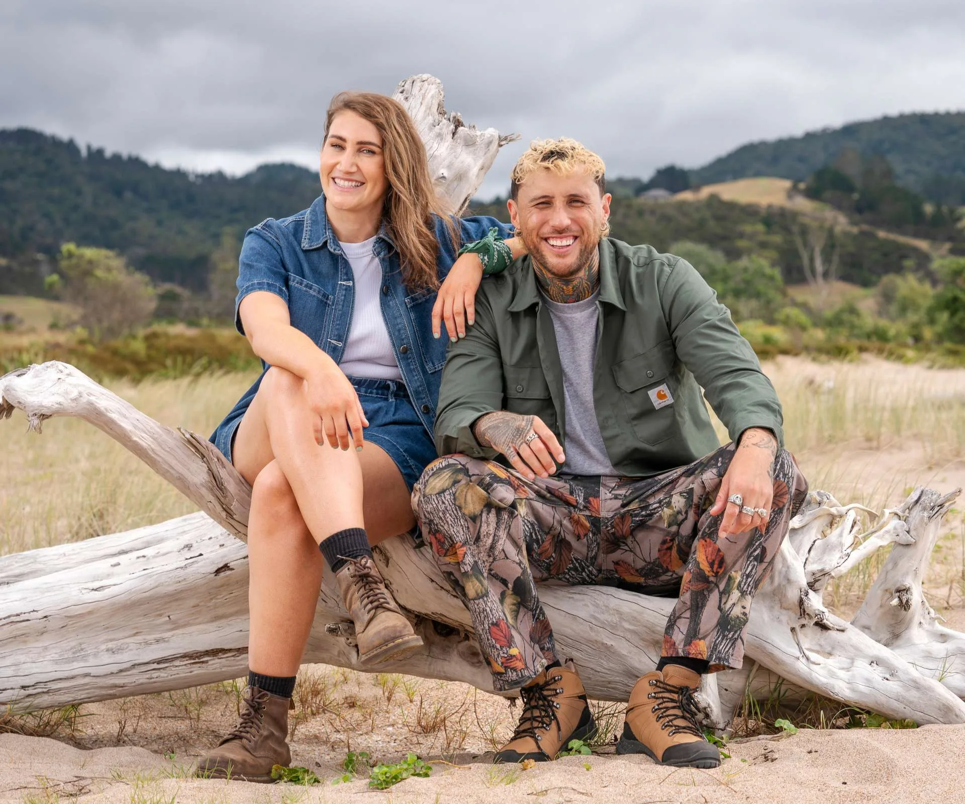 Celebrity Treasure Island hosts Lance and Bree sitting on driftwood on a beach