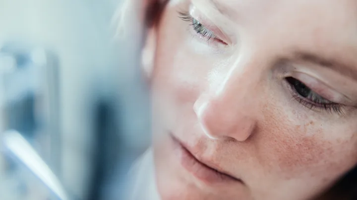 Close-up of a person's face, focusing on the eye and freckles, with a blurred background.