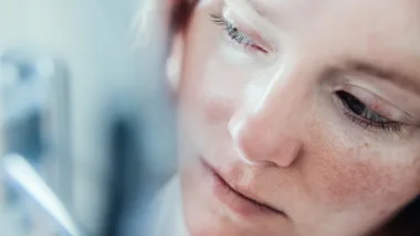 Close-up of a person's face, focusing on the eye and freckles, with a blurred background.