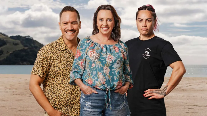 Three people smiling on a beach; one wears a leopard print shirt, another a floral blouse, and the third a black T-shirt.