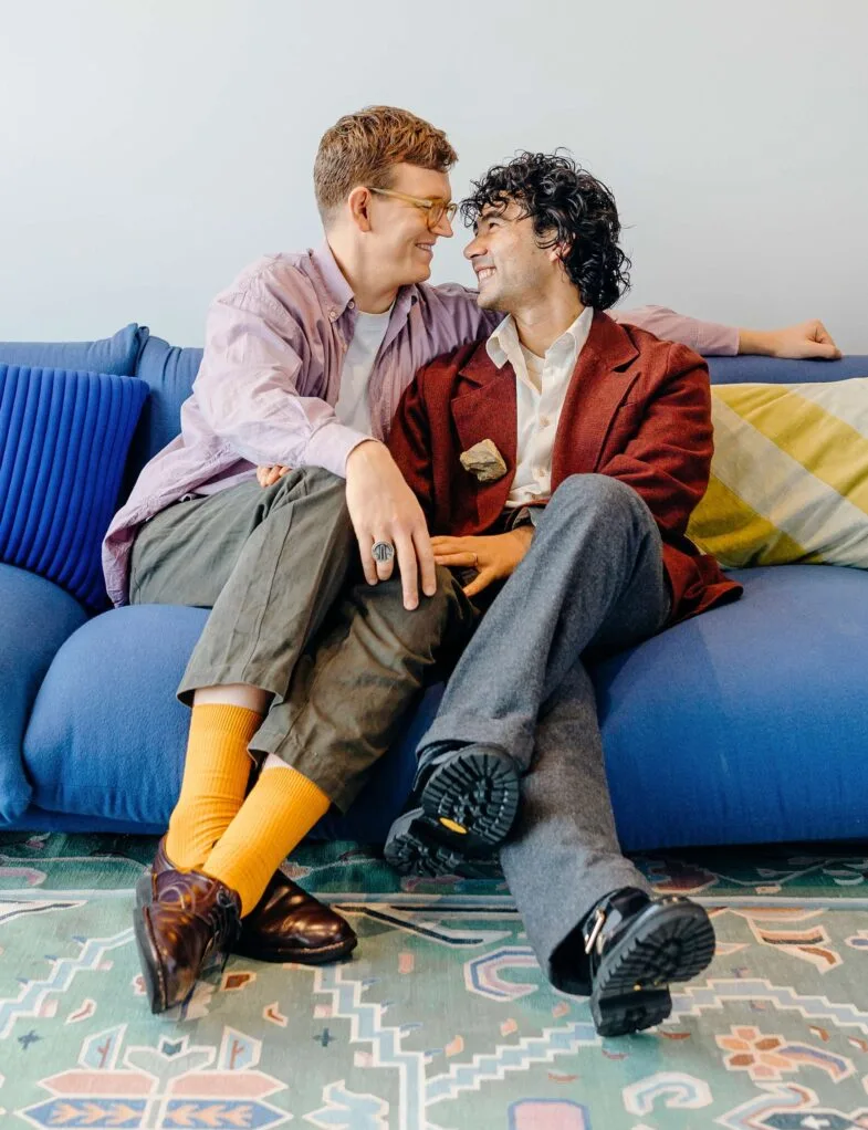 Chris and Micheal looking at each other closely and smiling while sitting on a blue couch together