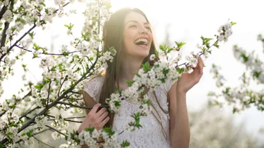 A woman standing amongst small white flowers wearing spring makeup