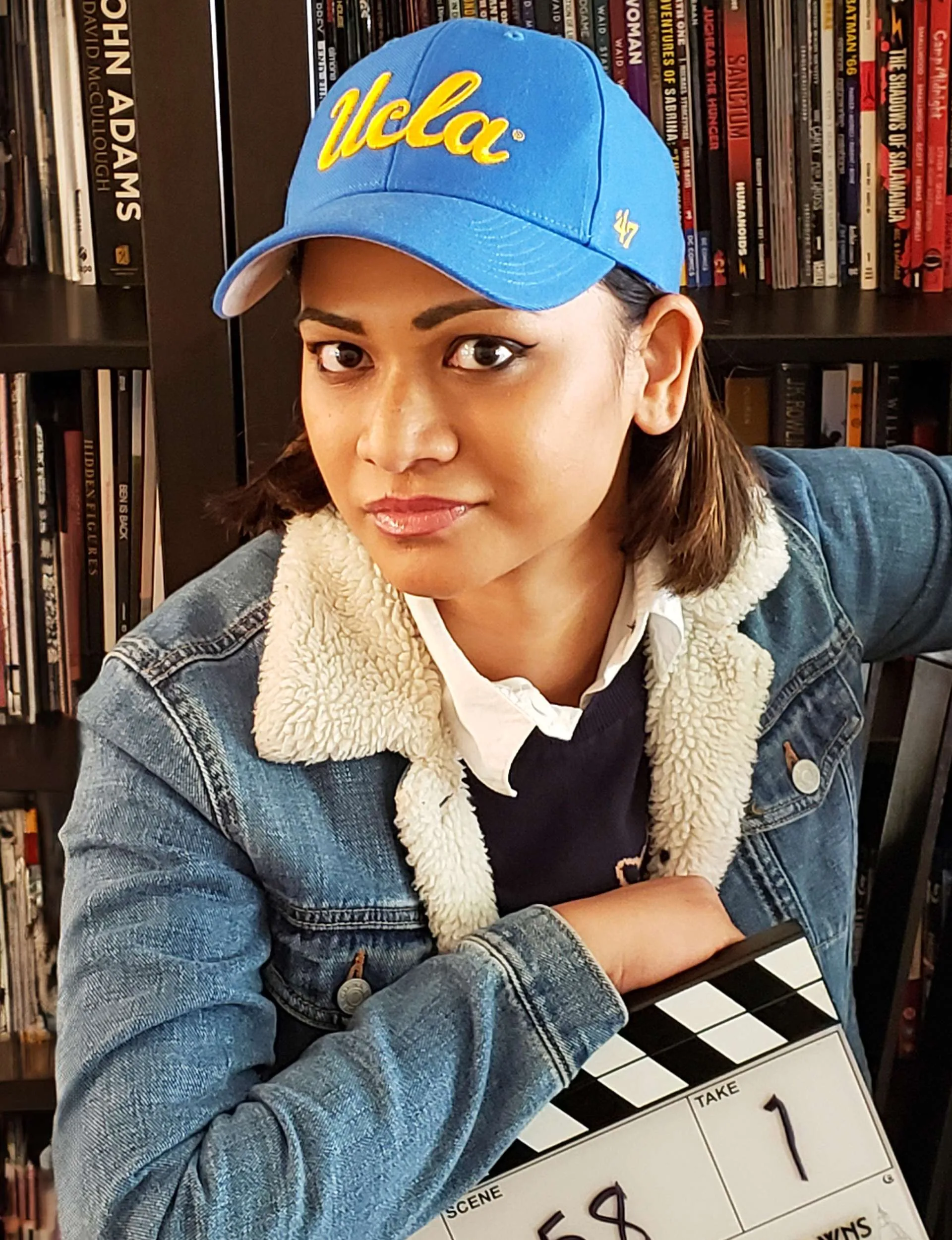 Shoshana Sachi leaning on a clap board in front of a bookshelf