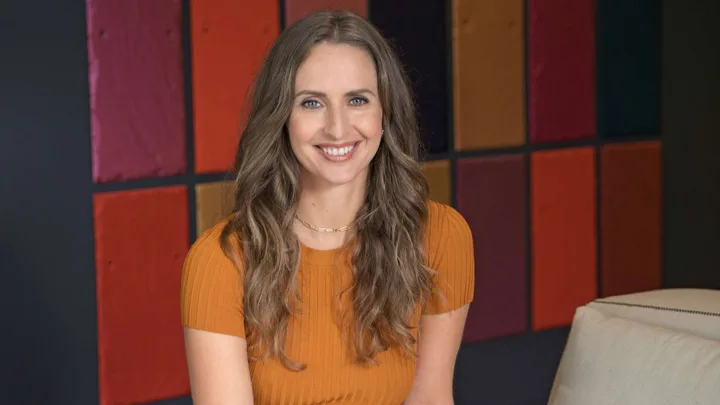 Fleur Saville smiling in front of a checkered background with different shades of red