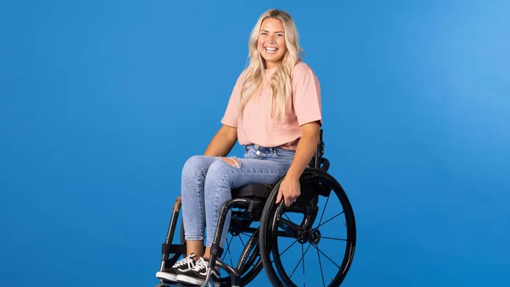 Casey smiling in her wheelchair in front of a blue background