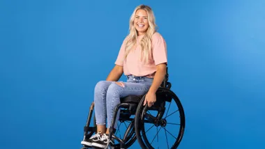 Casey smiling in her wheelchair in front of a blue background