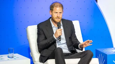 Prince Harry speaking into a microphone on stage in front of a blue background