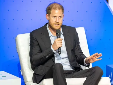 Prince Harry speaking into a microphone on stage in front of a blue background