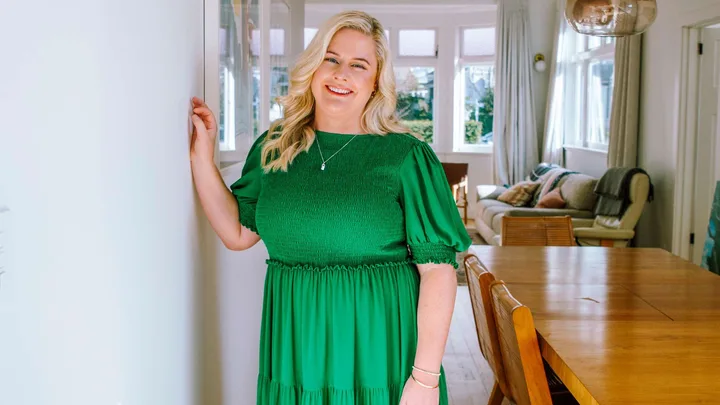 Rikki Swannell in a lime green dress leaning against a white wall