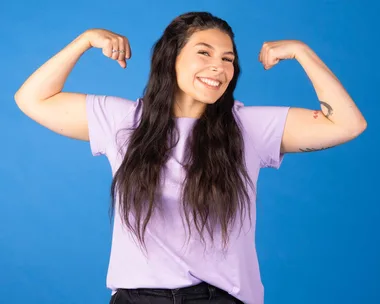 Zazi Gohar flexing her muscles in front of a blue backdrop