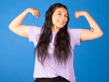 Zazi Gohar flexing her muscles in front of a blue backdrop