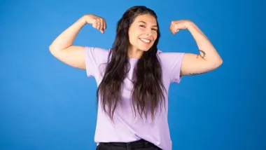Zazi Gohar flexing her muscles in front of a blue backdrop