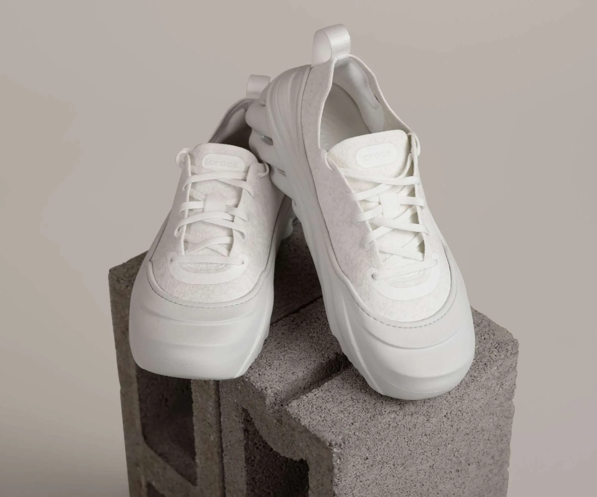 A pair of white crocs sneakers propped up on a cinderblock