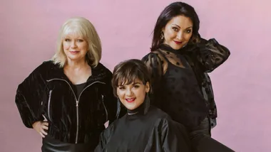 The Lady Killers all wearing black in front of a lilac backdrop