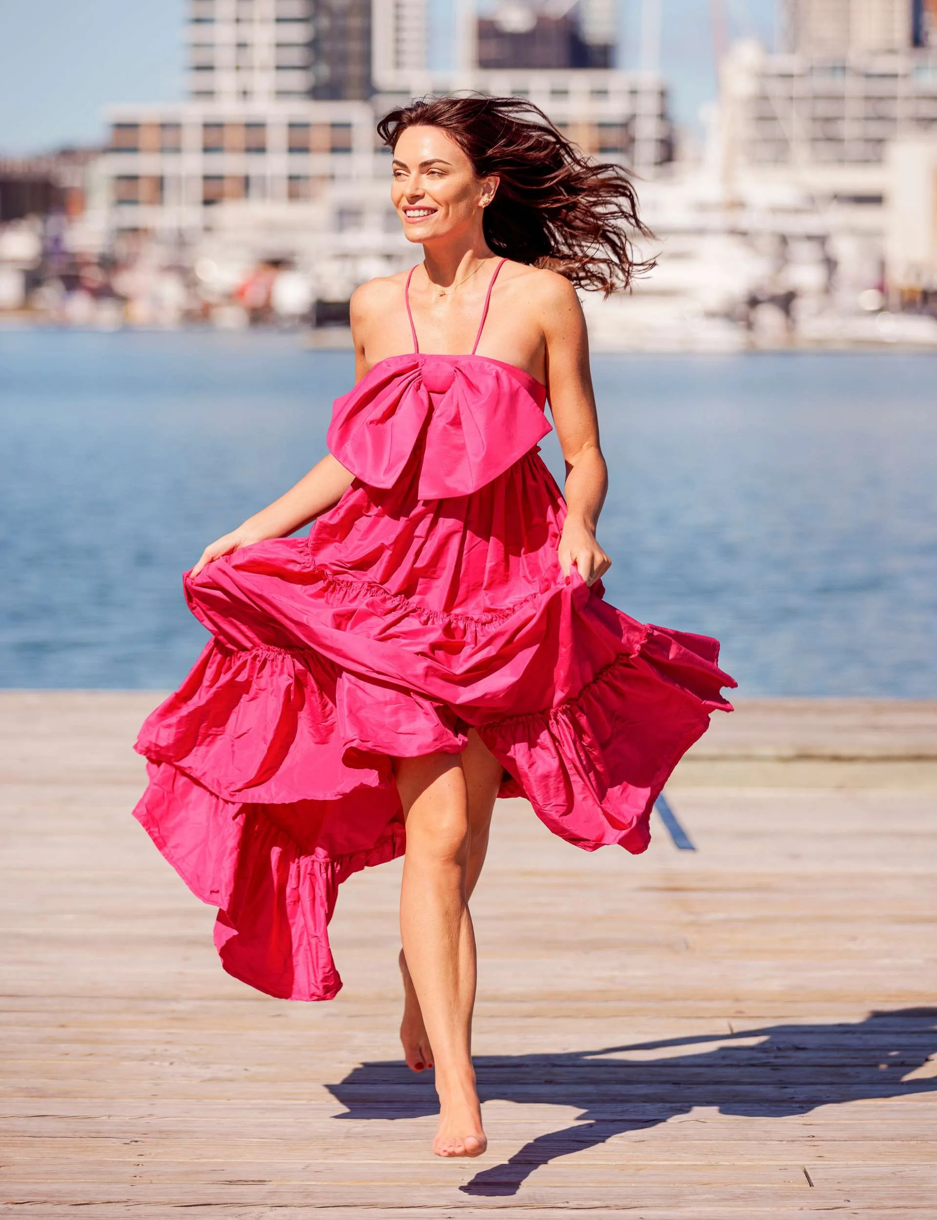 Katie Flood running on Auckland's waterfront with her hair and dress blowing behind her
