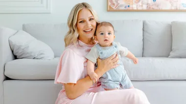 Hayley Holt holding baby Kingston in front of the couch