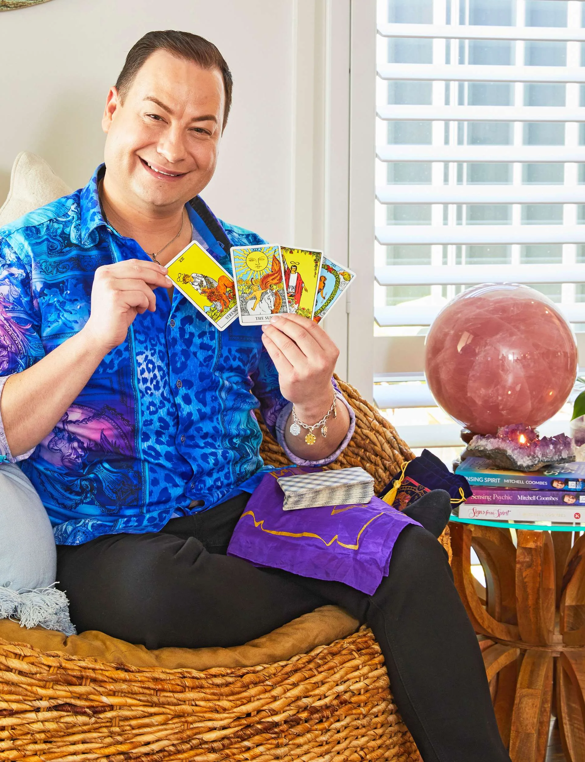 medium Mitchell Coombes sitting beside a stack of his books, holding tarot cards