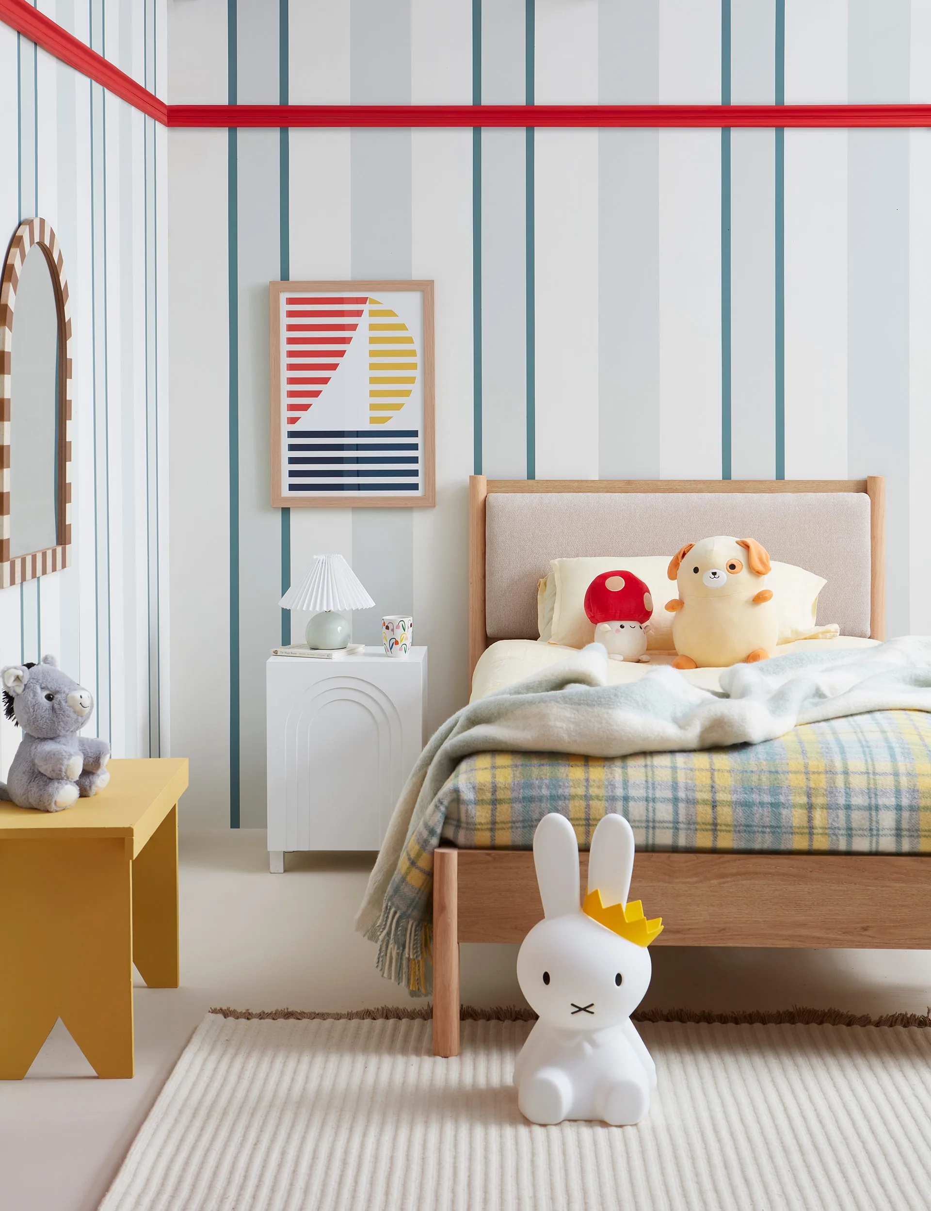 A kids bedroom with blue and white painted stripes. Red, yellow and blue striped sailboat artwork on wall, single bed with stuffed toys