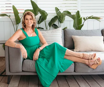 Jayne Kiely in green dress sitting on outdoor lounge with green fern plants in background