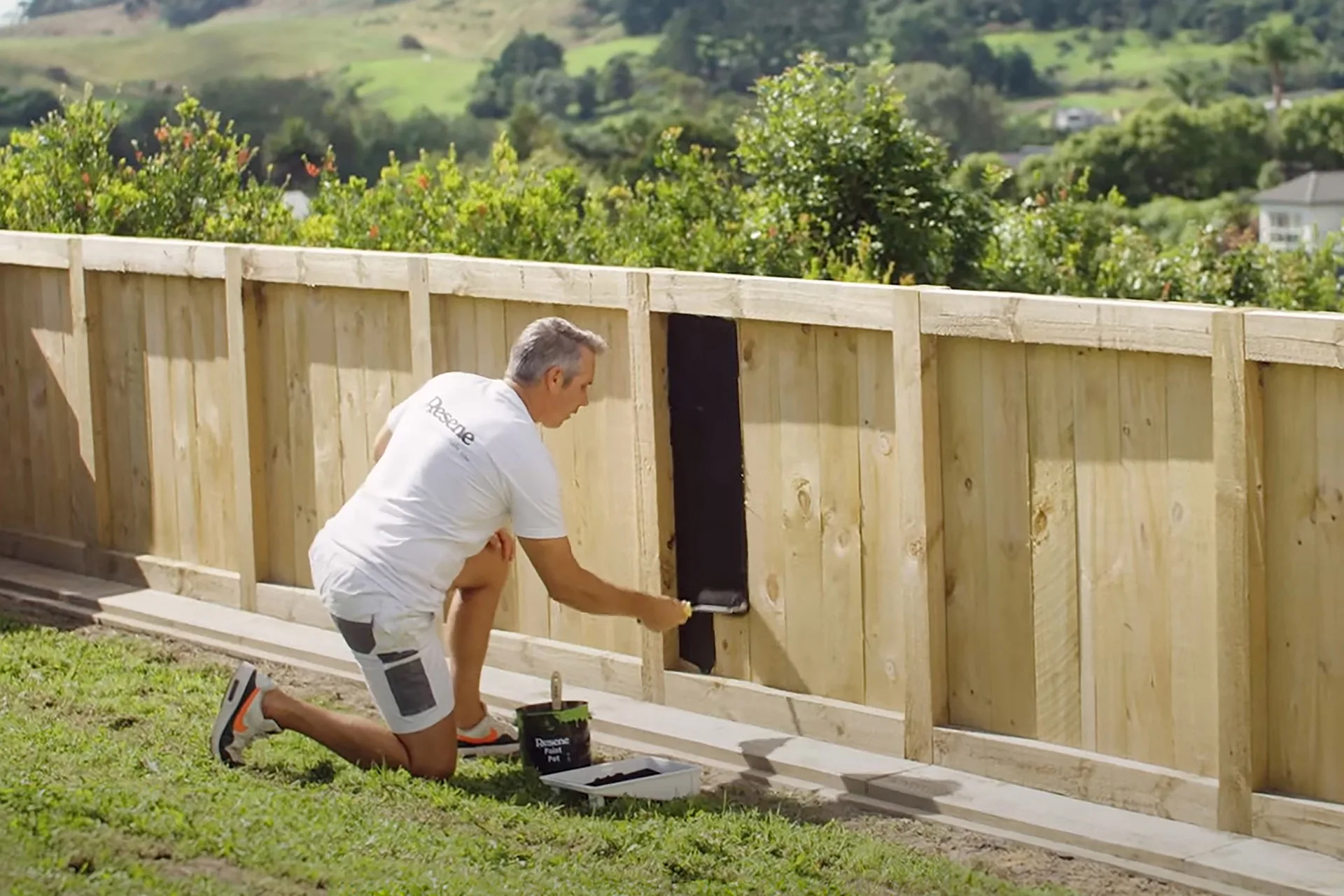 Man painting a fence. This fence is being stained with Resene Waterborne Woodsman CoolColour in Resene Pitch Black