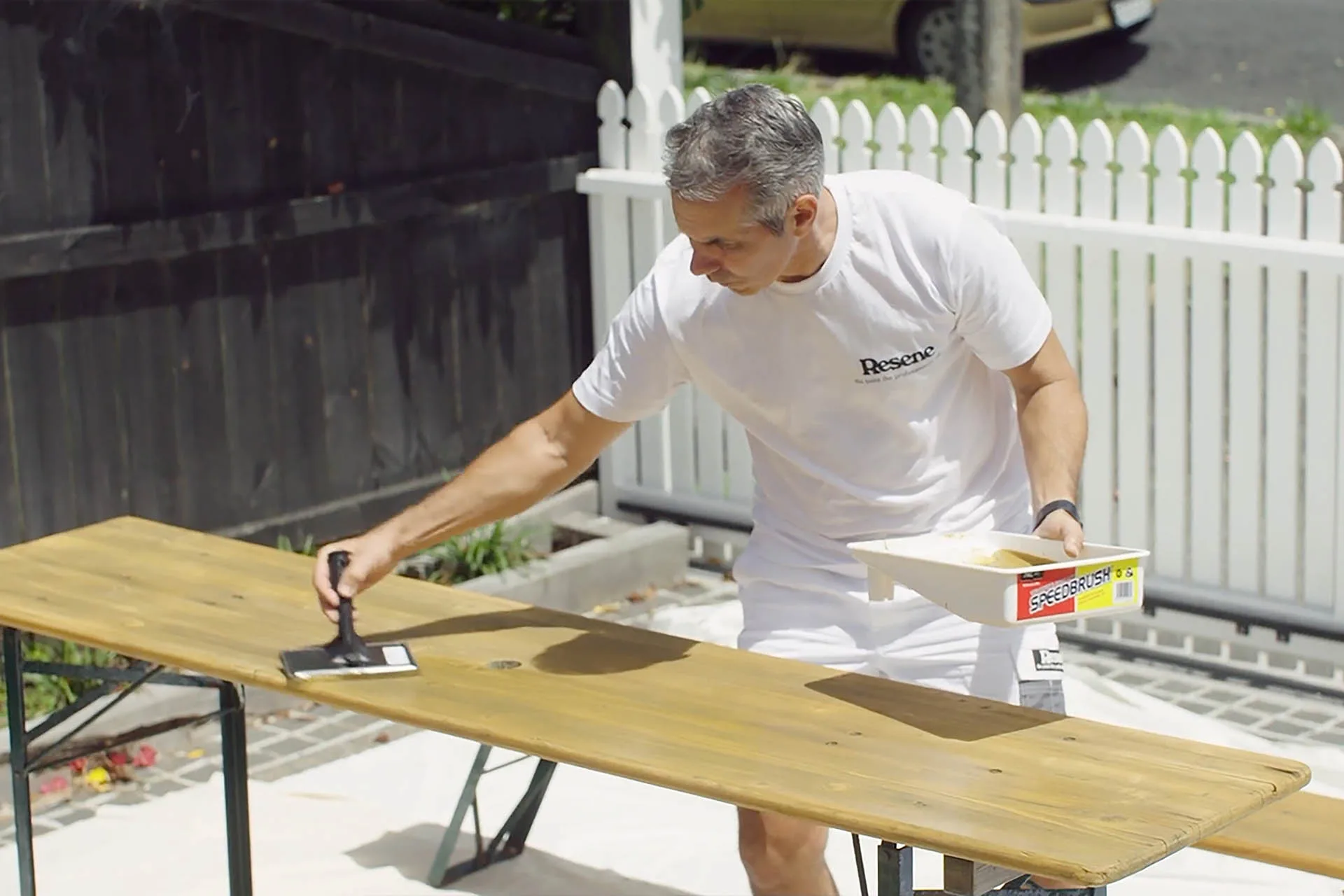 Man staining an outdoor table with Resene Woodsman Wood Oil Stain in Resene Natural