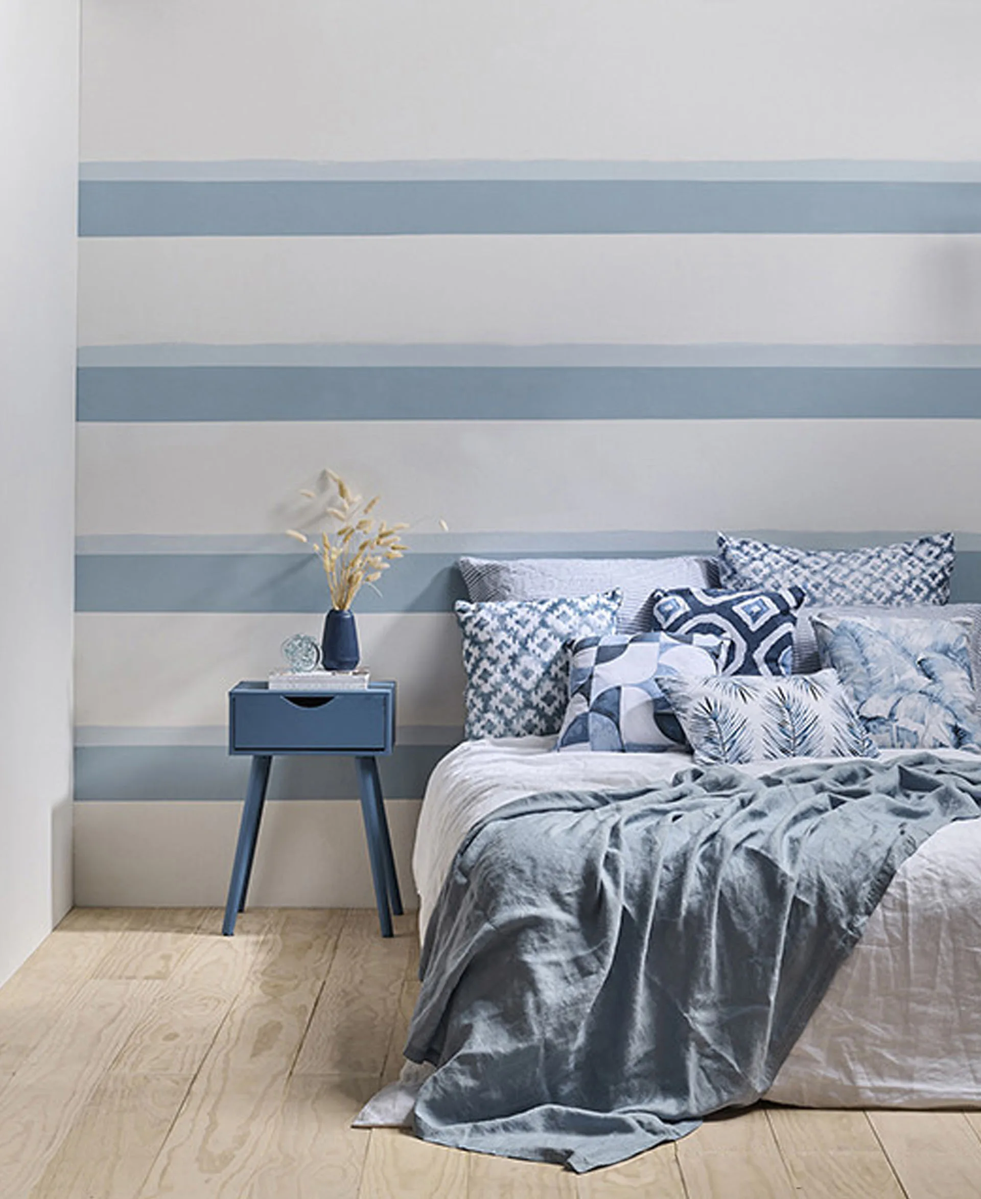 Bedroom wall painted with blue and white stripes, bed with blue bedding and blue bedside table