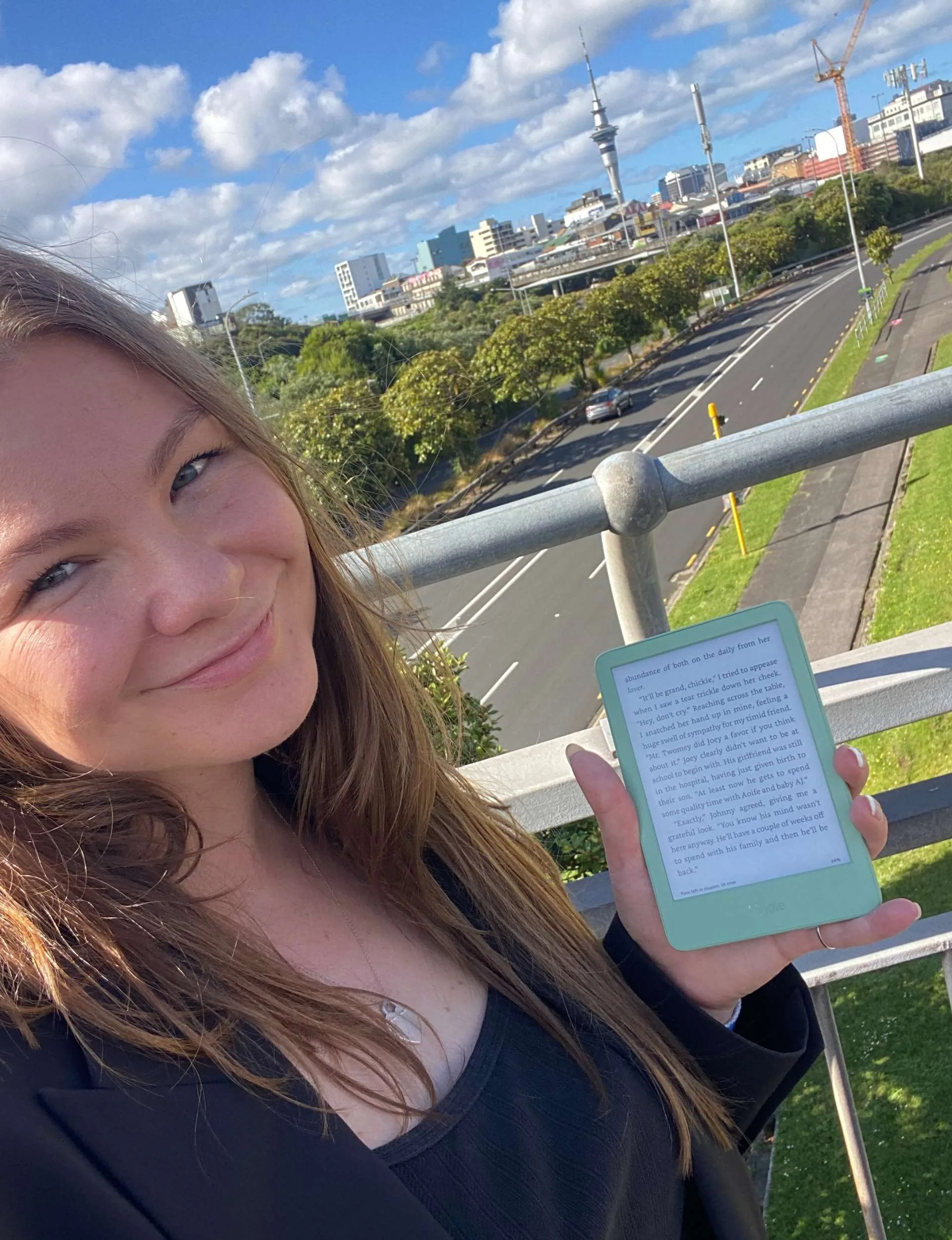 Mae holding up the Kindle on a ridge in front of the Auckland Sky Tower