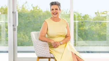 Paula smiling in a yellow dress, sitting on an armchair