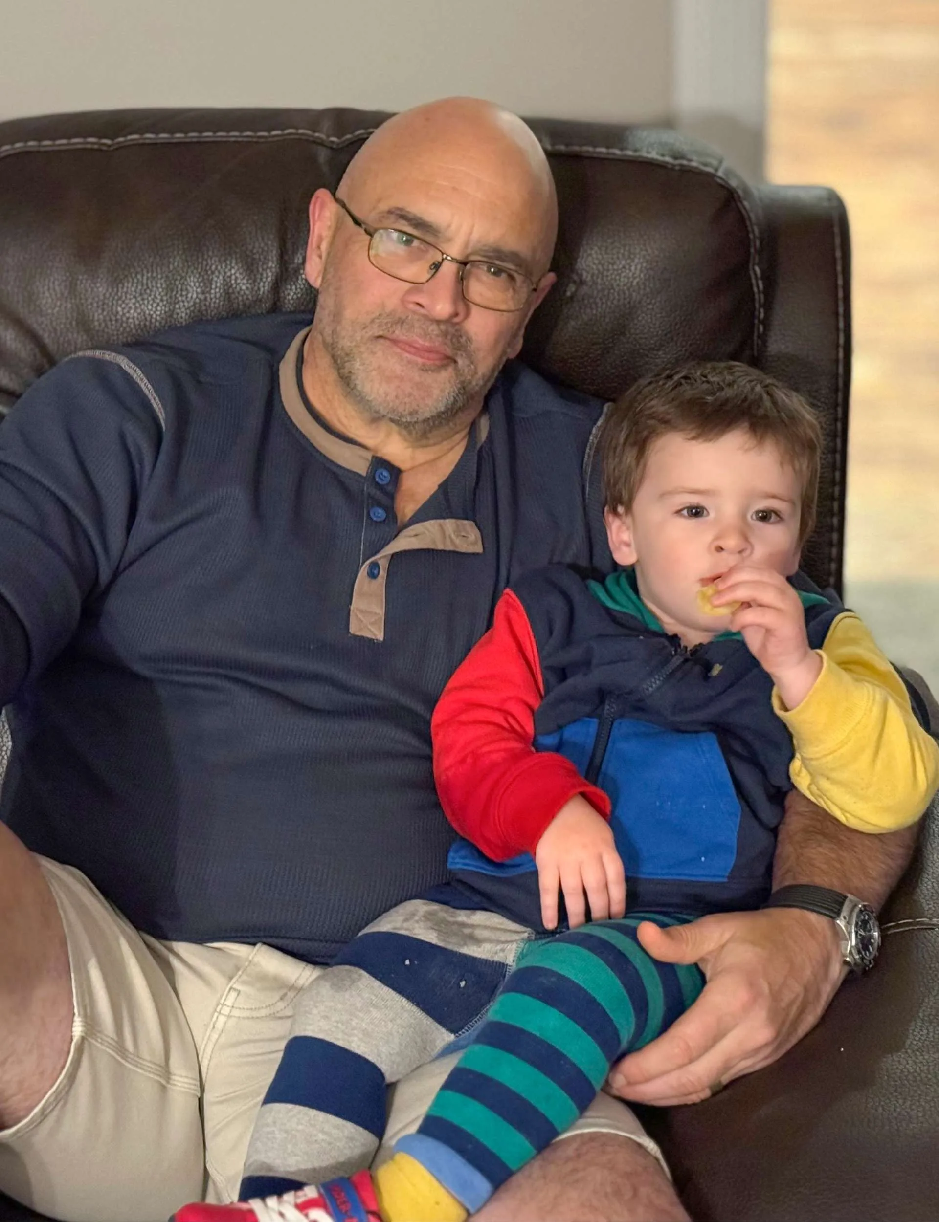 Grant sitting on a couch holding his grandson