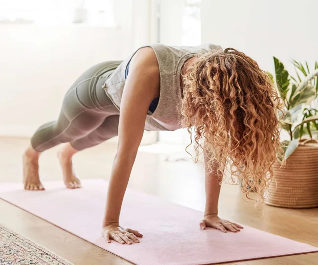 A woman doing push ups on a yoga mat at home