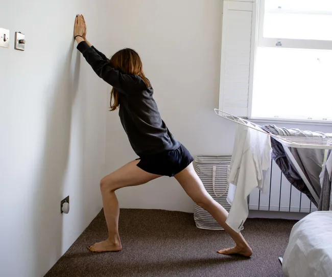 Woman stretching against a wall in a room with laundry drying on a rack.