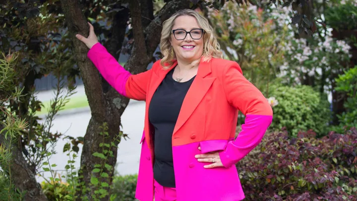 Jess van Slooten leaning against a tree in a bight pink and red suit
