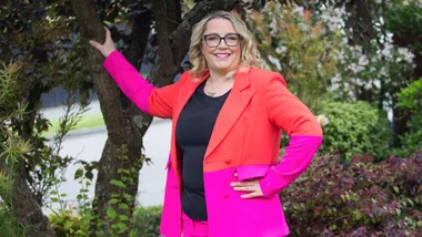 Jess van Slooten leaning against a tree in a bight pink and red suit