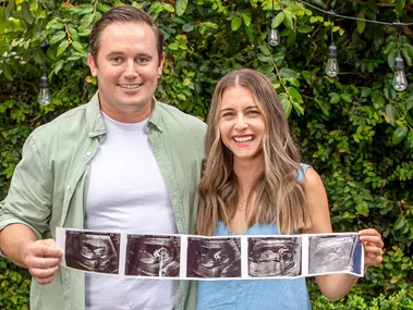 Kiwi couple Emma and Travis holding up the ultrasound images of their surrogate baby