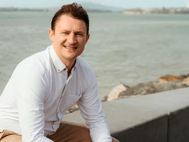 Hamish Williams sitting on a ledge near a beach