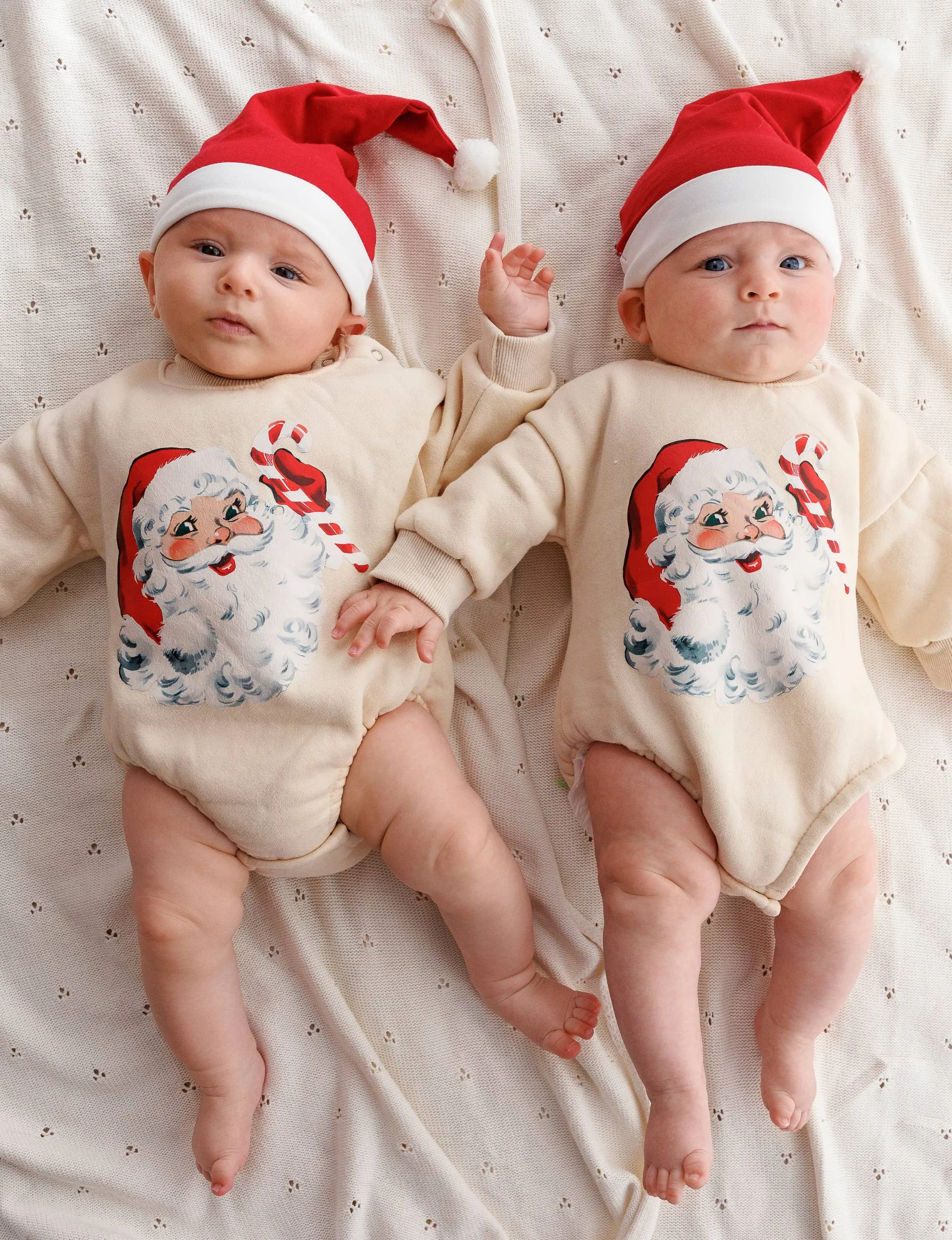 Walter and Darcy laying beside each other in matching Santa onesies and Santa hats