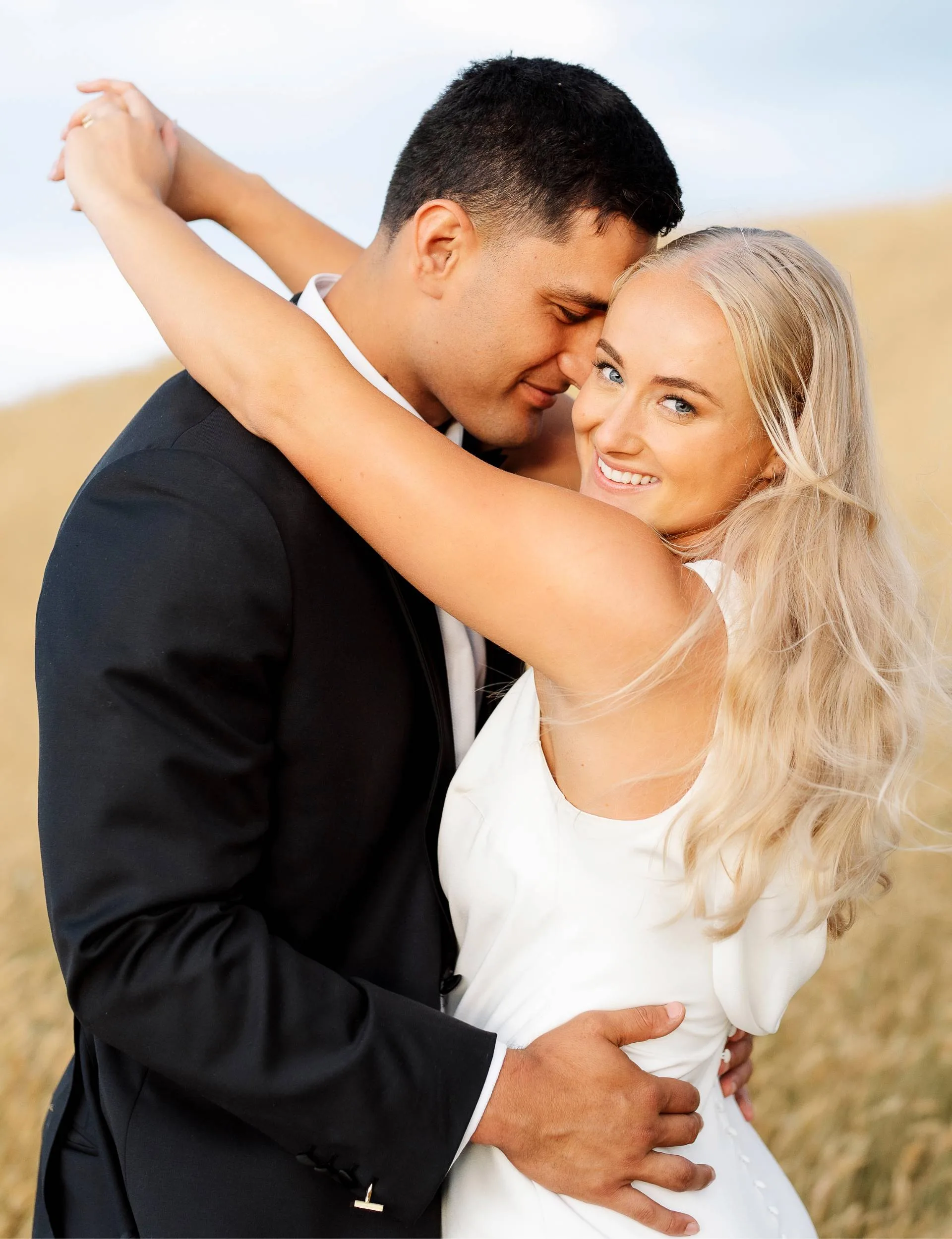Grace smiling at the camera as her husband nuzzles into her neck