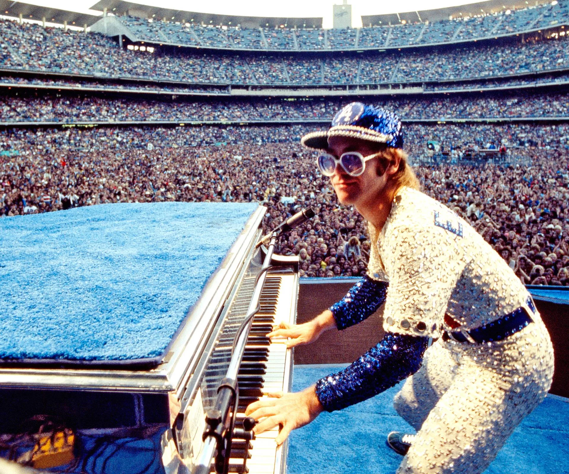 Elton John performing in a fully sequined outfit in front if thousands of people
