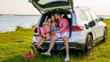 A family all sitting in the boot of their car playing games on a break from their road trip